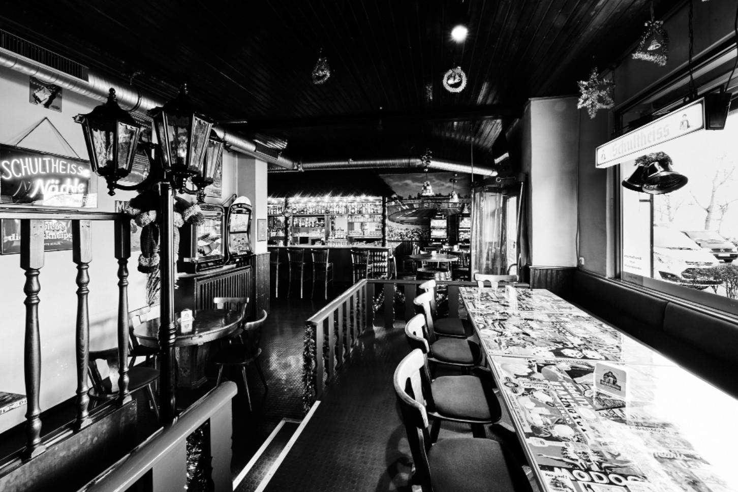 Eine Bar in Schwarz-Weiß mit Hockern entlang einer Theke und dekorativen Lampen.