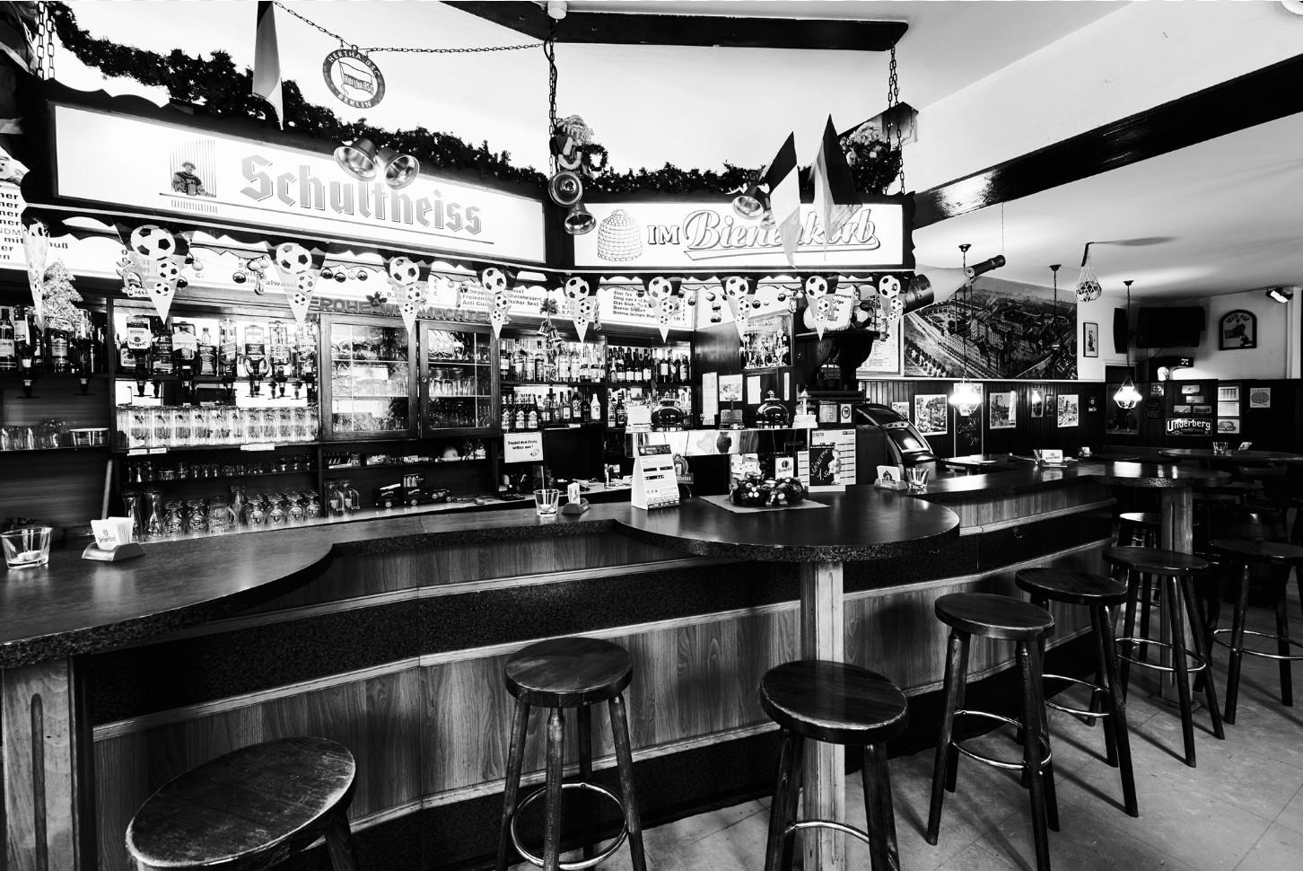 Eine Bar mit vielen Sitzhockern und einer Theke voller Getränke ist zu sehen. Dekorationen und Spiegel schmücken den Raum.