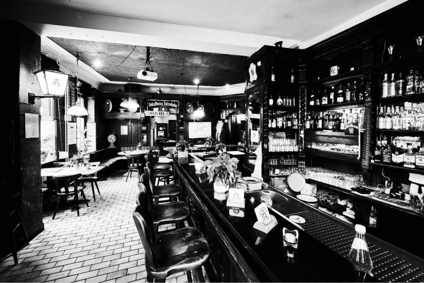 Ein Schwarz-Weiß-Foto zeigt das Innere einer traditionellen Bar mit Holzmobiliar und einer großen Getränkeauswahl.