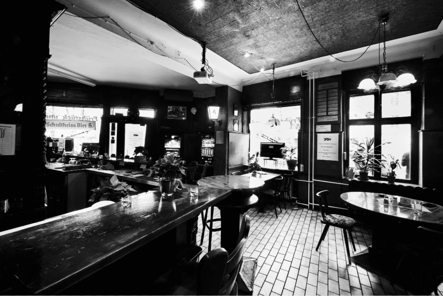 Ein schwarz-weiß Foto zeigt das Innere einer traditionellen Bar mit Tischen und Theke.