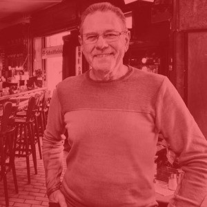 Ein lächelnder älterer Mann steht in einem Außencafé.