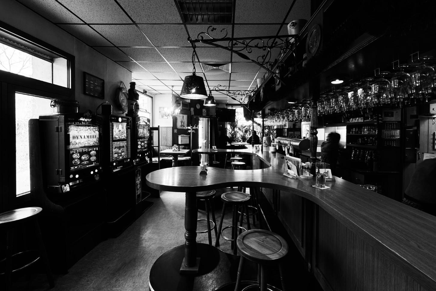 Schwarz-weiß Foto einer Bar mit Tischen, Hockern und Spielautomaten.