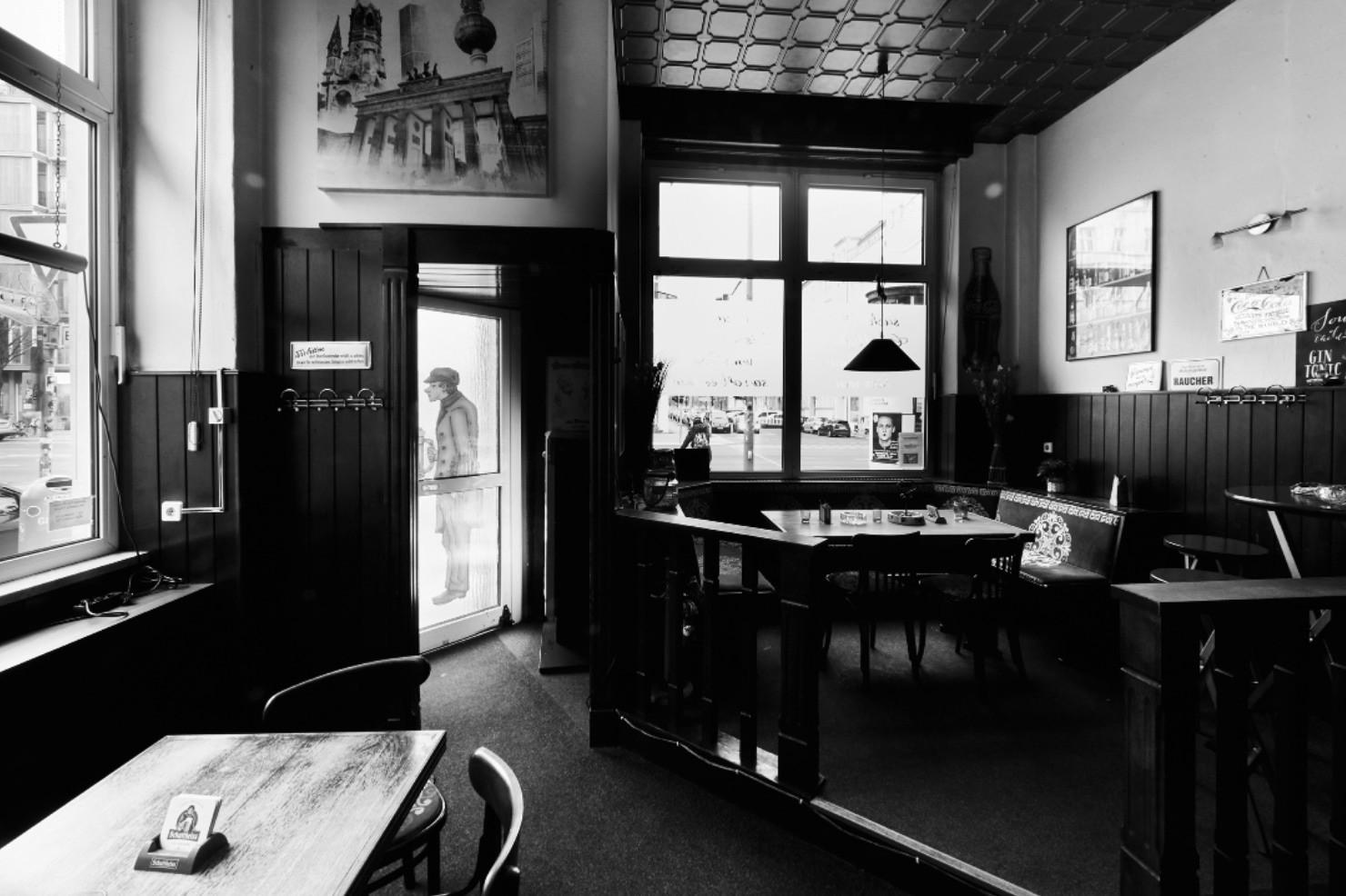 Schwarz-weiß Foto eines leeren Cafés mit Tischen und Stühlen, Blick zur Eingangstür.