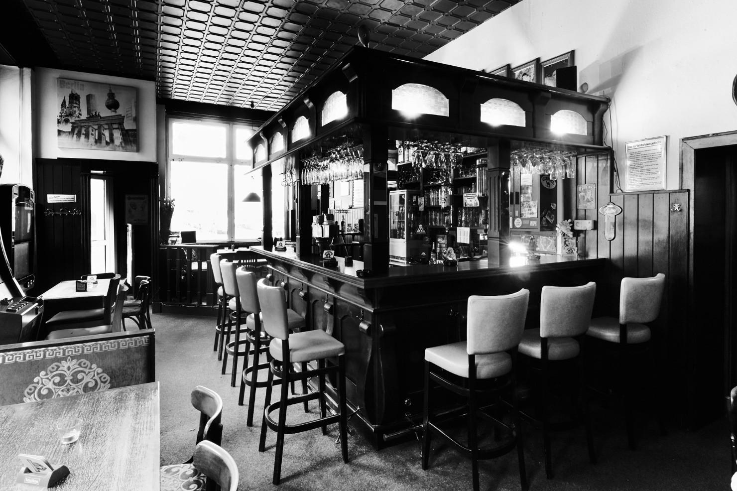 Eine traditionelle Bar mit Tresen, Barhockern und beleuchteten Regalen voller Getränke.