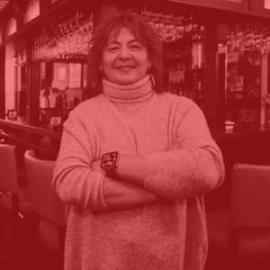 Eine Person steht lächelnd mit verschränkten Armen in einer Bar.