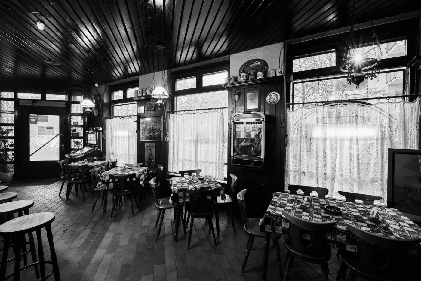 Ein historisches Kaffeehaus mit holzvertäfelten Wänden und dekorativen Lampen ist abgebildet. Es gibt mehrere Tische und einen alten Jukebox-Automaten.