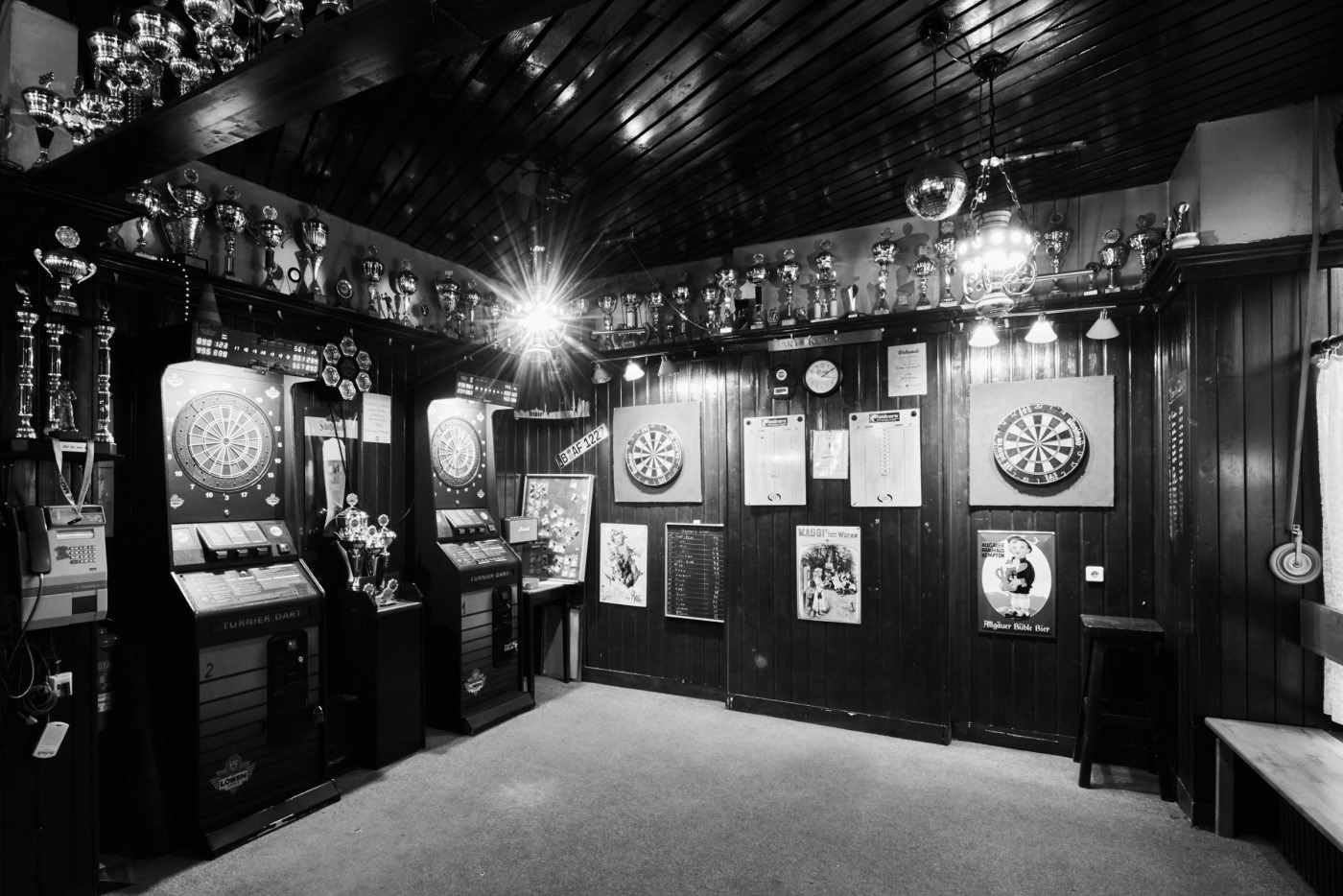 Innenansicht eines Darts-Vereinsheims mit Pokalen an der Wand und Dartscheiben.