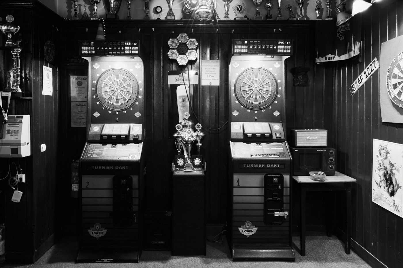 Zwei Dartscheiben an der Wand zwischen Dart-Automaten, Trophäen und Pokalen darüber.