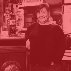 Eine lächelnde Frau steht lehnt an einer Bar in einem Gasthaus.