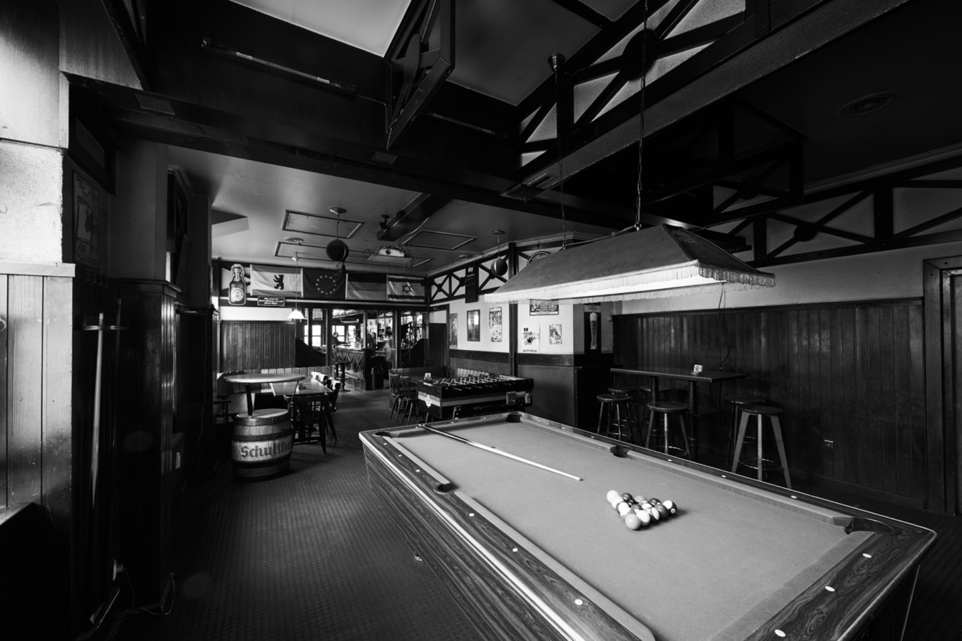 Innenansicht einer traditionellen Bar mit Billardtisch und Tischen, alles in Schwarz-Weiß.