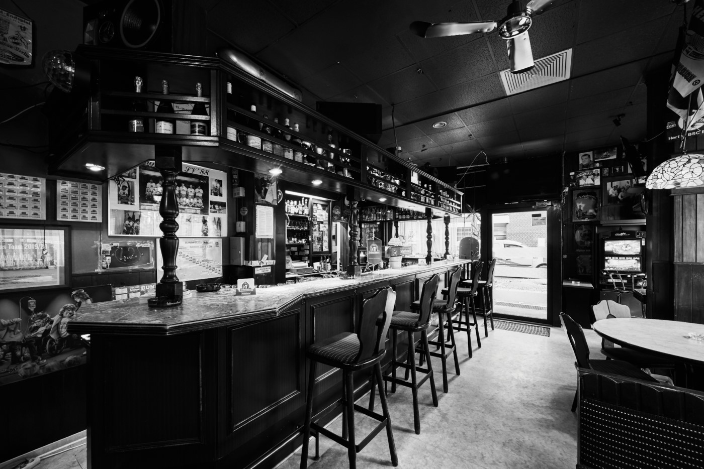 Eine leere Bar mit Theke und Hockern in Schwarz-Weiß Fotografie; das Innere ist rustikal dekoriert.
