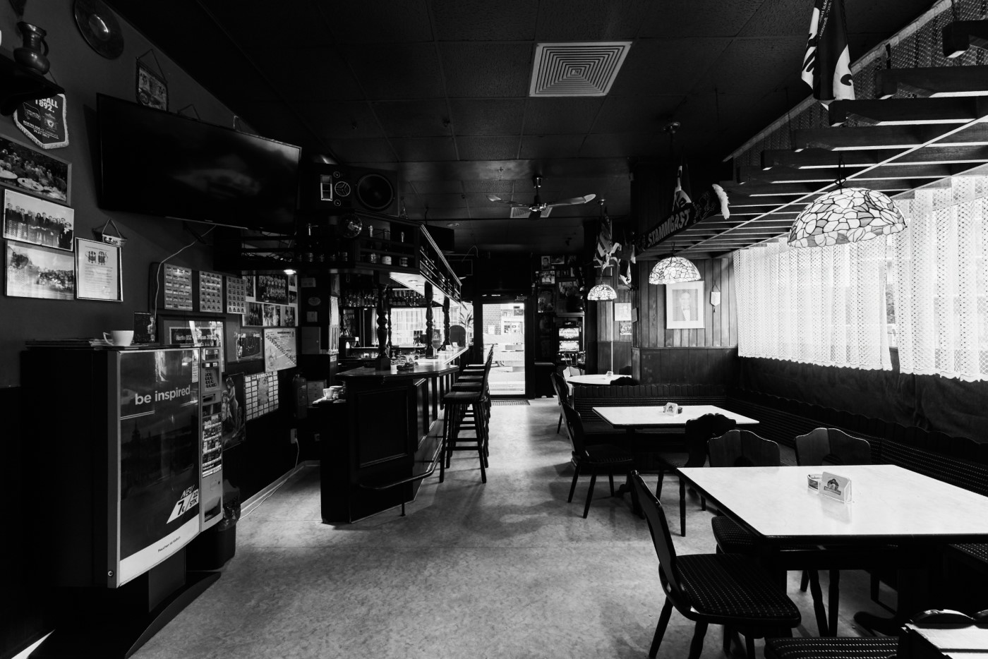 Innenansicht einer leeren Bar in Schwarz-Weiß mit Tischen, Stühlen und einer Theke.